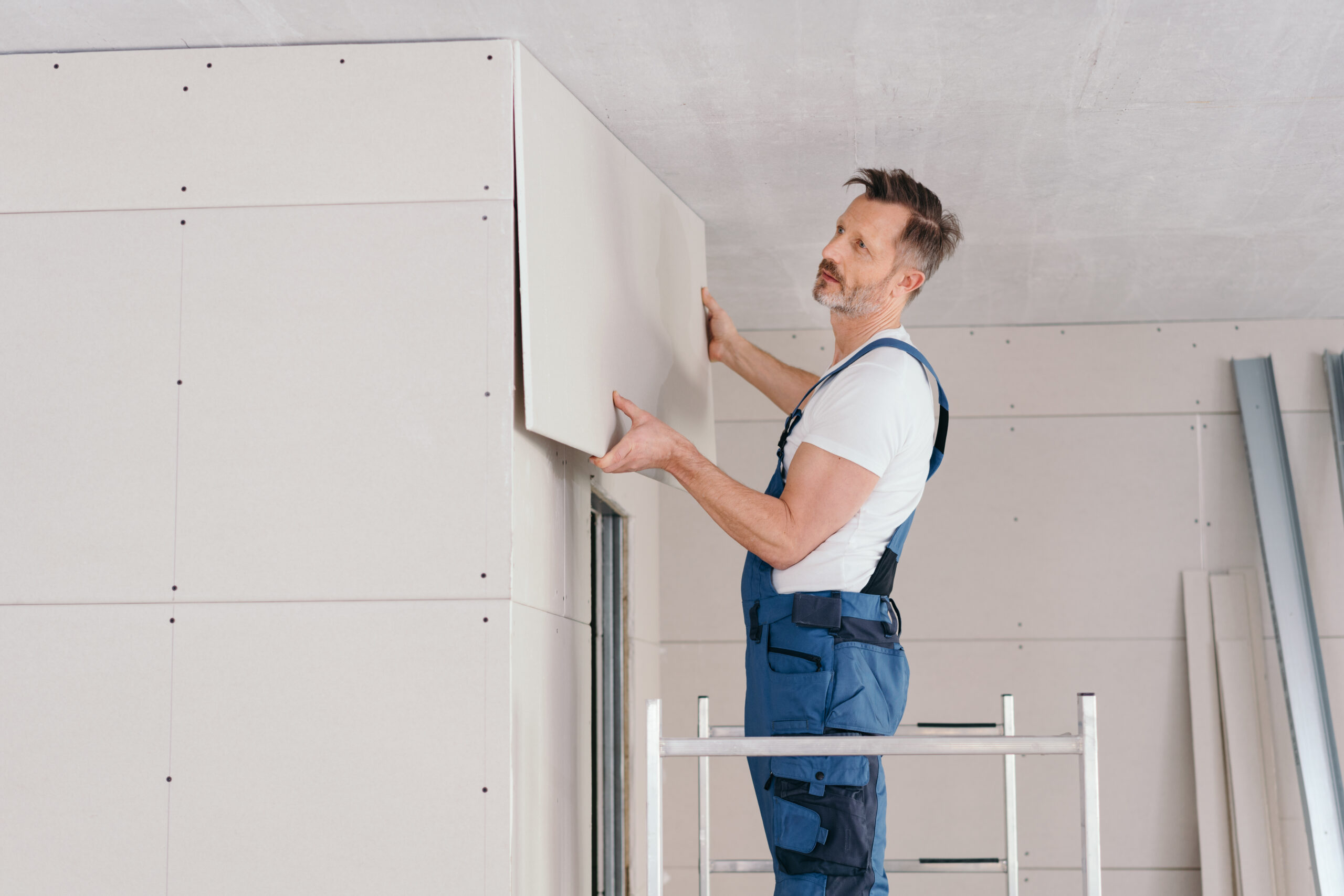 Builder or handyman fitting wall cladding inside a new build house standing on low metal scaffolding